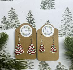 two christmas tree shaped earrings on top of a card with pine trees in the background