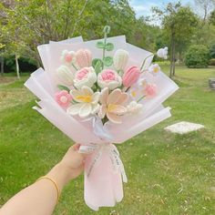 a person holding a bouquet of flowers in their hand with grass and trees in the background