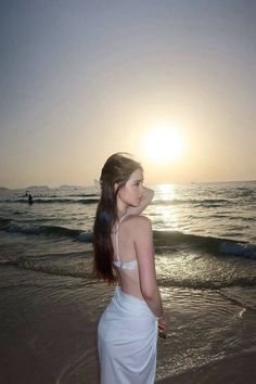 a woman standing on top of a sandy beach next to the ocean at sun set