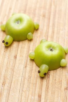 two green apples shaped like animals sitting on top of a wooden table