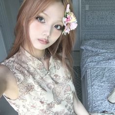 a woman with long red hair and flower in her hair posing for a photo next to a bed