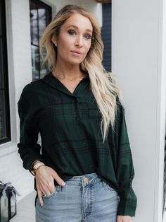 a woman wearing a green shirt and jeans standing in front of a white house with her hand on her hip