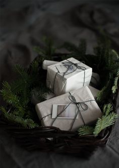 three wrapped presents in a wicker basket on a bed with pine branches and needles