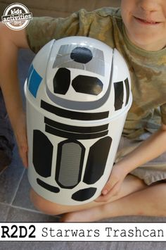 a young boy sitting on the floor holding a toy r2d2 trash can