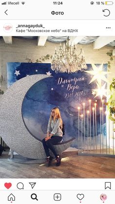 a woman sitting on top of a large moon in front of a chandelier