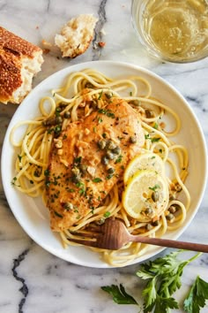 a white plate topped with chicken and pasta next to bread on top of a marble counter