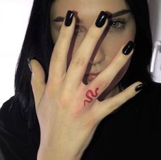 a woman with black nails holding her hand up to her face and the letter s painted on her fingers