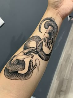 a hand with a snake tattoo on it's arm and the hands are holding an object