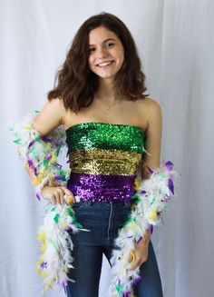 a woman in a green and purple top with feathers on her arms, smiling at the camera