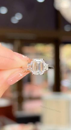 a woman's hand holding an engagement ring in front of her face with the center diamond on it