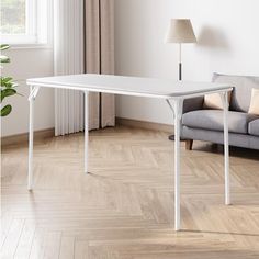 a white table sitting on top of a hard wood floor next to a gray couch