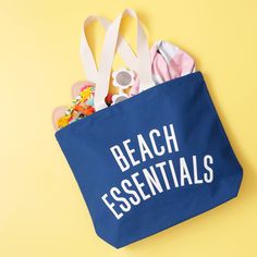 a blue beach bag with the words beach essentials written on it and various items inside