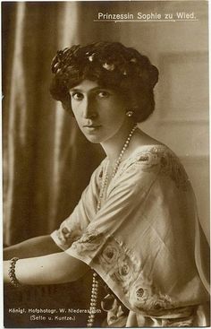 an old black and white photo of a woman with pearls on her head, sitting in a chair