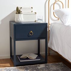 a blue nightstand with an open book on it next to a white bed in a bedroom