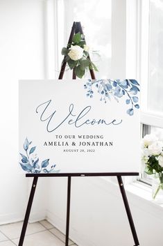 a welcome sign sitting on top of a easel next to a vase with flowers