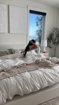 a woman laying on top of a white bed in a bedroom next to a window