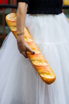 a woman in a white skirt holding a long loaf of bread