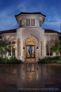 the front entrance to a luxury home at night with palm trees and blue skies in the background