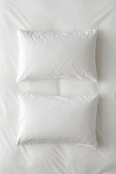 three pillows on top of a bed with white sheets