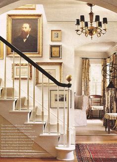 a staircase leading to a living room with pictures on the wall and chandelier