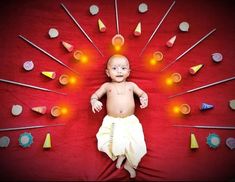 a baby sitting on top of a red blanket surrounded by pins and needles in the shape of a peacock