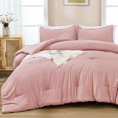 a bed with pink comforter and pillows in a room next to a window,