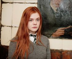 a woman with long red hair standing in front of a painting and looking at the camera