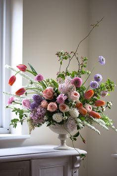 a vase filled with lots of different colored flowers on top of a table next to a window