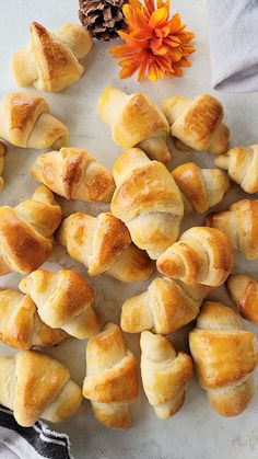 several croissants on a white surface next to an orange flower and pine cone