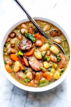 a bowl of soup with sausage, beans and broccoli on a marble table