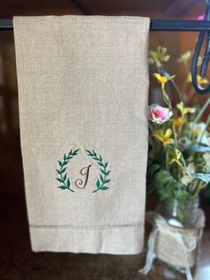 an embroidered monogrammed towel hangs on a rack next to a vase with flowers