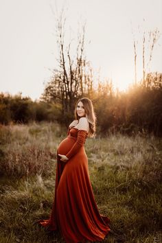 a pregnant woman in an orange dress poses for the camera with her hands on her hips