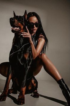 a woman is posing with her dog in front of a gray background and wearing black boots