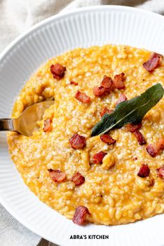 a white bowl filled with corn and bacon on top of a table next to a spoon