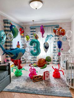 a room filled with lots of balloons and animals hanging from the ceiling next to a crib