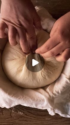 two hands knead an uncooked piece of bread on top of a wooden table