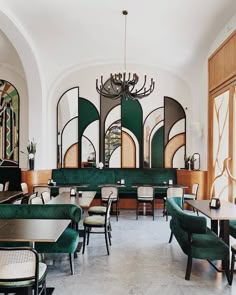 the interior of a restaurant with green velvet booths and white tables, chandeliers and chairs