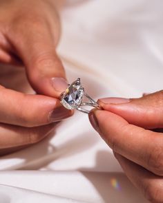 two hands holding a diamond ring on top of a white sheet