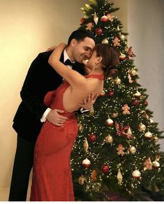 a man and woman hugging in front of a christmas tree