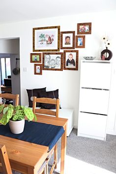 a dining room table and chairs with pictures on the wall above it, along with a potted plant