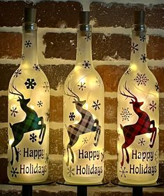 three wine bottles with christmas lights on them sitting next to each other in front of a brick wall