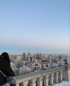 a woman standing on top of a tall building next to a snow covered ground with buildings in the background