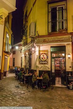 people sitting at tables in front of a building on a cobblestone street corner