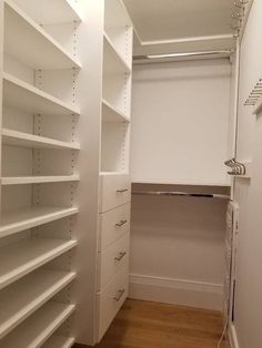 an empty walk in closet with white shelving and wood flooring on the side