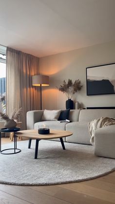 a living room filled with furniture next to a large window and a wooden table on top of a white rug