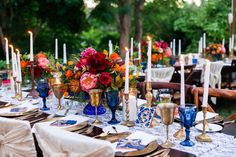 the table is set with blue and gold dishes, candles, and flowers in vases