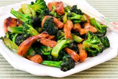 a white plate topped with broccoli and meat next to chopsticks on a table