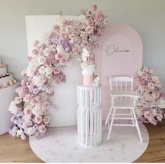 a white table topped with pink flowers next to a chair and wall covered in fake flowers