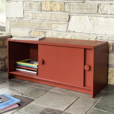 a red cabinet sitting on top of a stone floor next to a book shelf with books