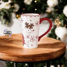 a red and white coffee cup sitting on top of a wooden table next to a christmas tree